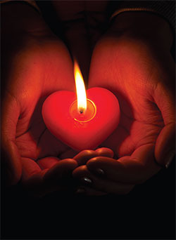 Two hands cupping a heart shaped lit candle